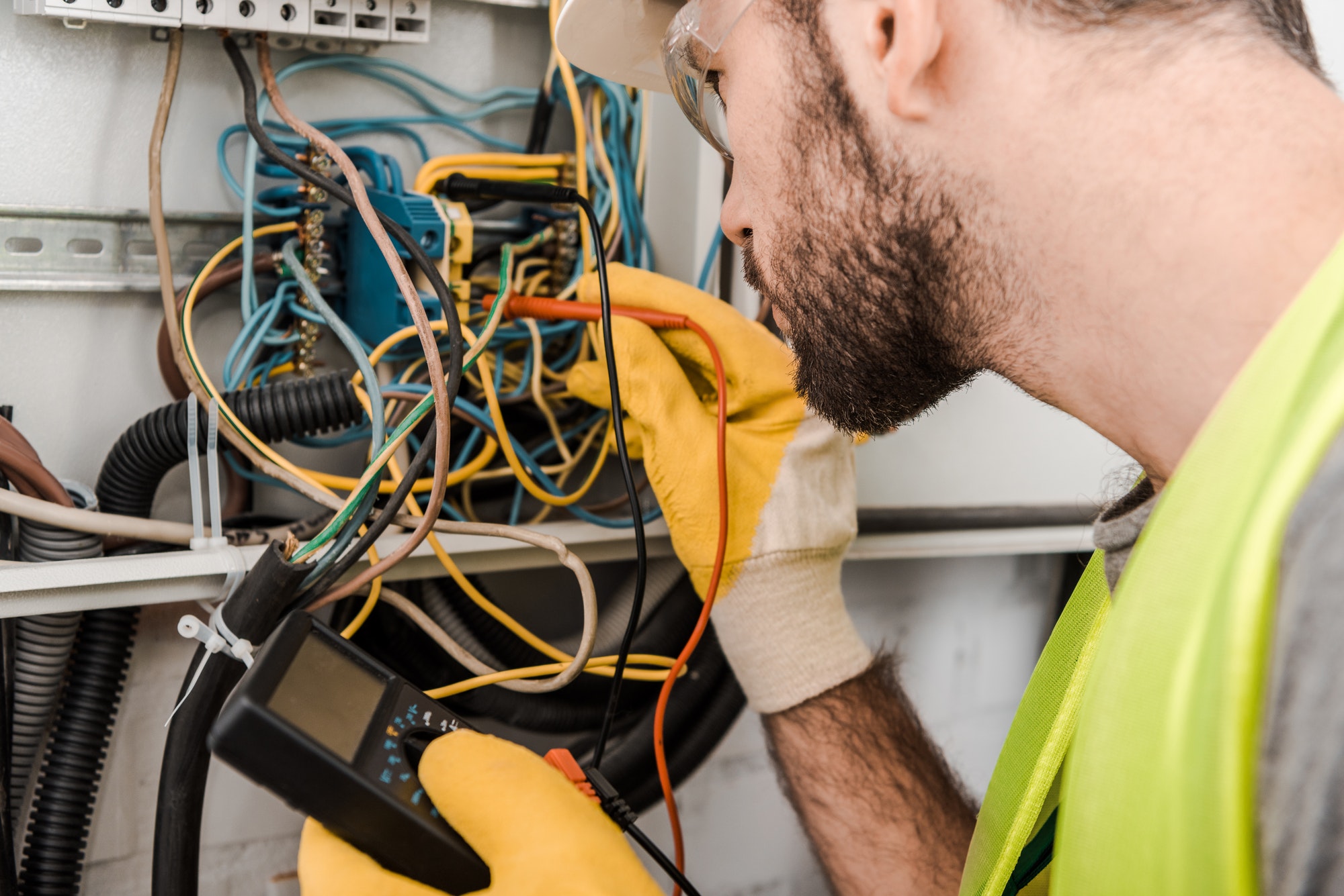 side view of electrician checking electrical box with multimetr in corridor